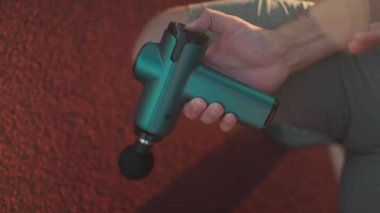 Athlete massages with percussion therapy gun to relieve pain of muscle aches after workout. Man massages his body with massage percussion device after training session. Muscle warming up with massager