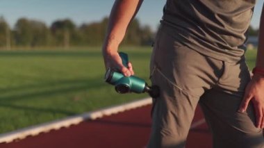 Athlete massages with percussion therapy gun to relieve pain of muscle aches after workout. Man massages his body with massage percussion device after training session. Muscle warming up with massager
