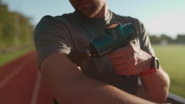 Athlete massages with percussion therapy gun to relieve pain of muscle aches after workout. Man massages his body with massage percussion device after training session. Muscle warming up with massager