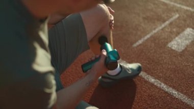 Athlete massages with percussion therapy gun to relieve pain of muscle aches after workout. Man massages his body with massage percussion device after training session. Muscle warming up with massager