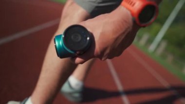 A male athlete massages muscles and tendons with a massage percussion device after a workout at the stadium. Sportsman uses electric massager gun in hand massaging the muscle. Sports recovery concept