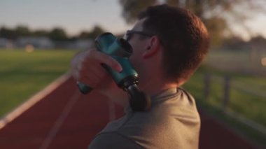 Athlete massages with percussion therapy gun to relieve pain of muscle aches after workout. Man massages his body with massage percussion device after training session. Muscle warming up with massager