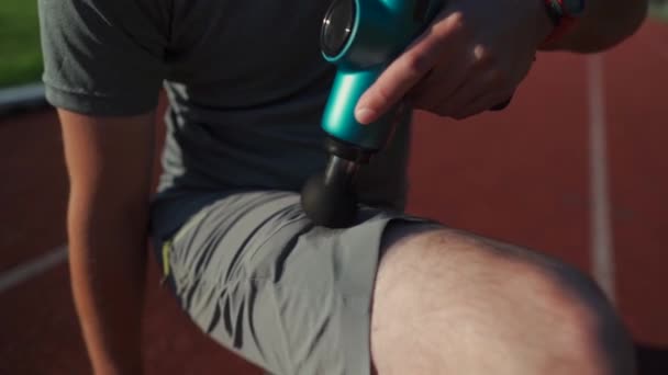 Athletic Male Massages Muscles Hand Massage Gun Recovering Stadium Running — стоковое видео