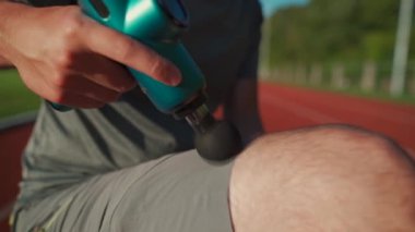 Athlete massages with percussion therapy gun to relieve pain of muscle aches after workout. Man massages his body with massage percussion device after training session. Muscle warming up with massager