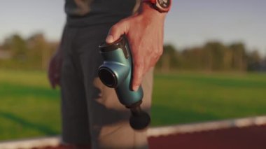 Athlete massages with percussion therapy gun to relieve pain of muscle aches after workout. Man massages his body with massage percussion device after training session. Muscle warming up with massager