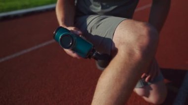 Athlete massages with percussion therapy gun to relieve pain of muscle aches after workout. Man massages his body with massage percussion device after training session. Muscle warming up with massager
