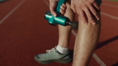 Athlete massages with percussion therapy gun to relieve pain of muscle aches after workout. Man massages his body with massage percussion device after training session. Muscle warming up with massager
