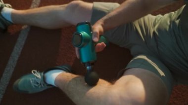 Athlete massages with percussion therapy gun to relieve pain of muscle aches after workout. Man massages his body with massage percussion device after training session. Muscle warming up with massager