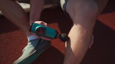 Athlete massages with percussion therapy gun to relieve pain of muscle aches after workout. Man massages his body with massage percussion device after training session. Muscle warming up with massager