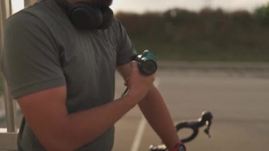 Cyclist athlete massages body with percussion therapy gun to relieve post workout muscle aches and pains on cycling workout. Massage percussion device after workout. Warming up muscles with massager