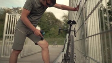Male cyclist massages muscles and tendons with massage percussion device after cycling workout. Athlete uses an electric pistol massager in his hand, massaging the muscles. Sports recovery concept. 
