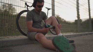 Male cyclist massages muscles and tendons with massage percussion device after cycling workout. Athlete uses an electric pistol massager in his hand, massaging the muscles. Sports recovery concept. 