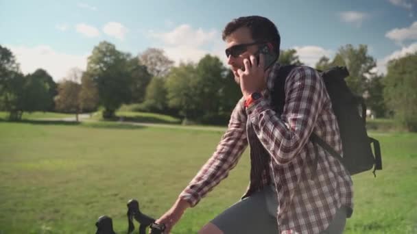 Чоловік Рюкзаком Їзді Велосипеді Парку Своєму Циклі Розмовляє Телефону Сонячну — стокове відео