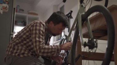 Bisikletçi, stüdyo dairesindeki bisiklete aksesuar takıyor. Adam evde bisiklet kuruyor. Erkek oturma odasındaki çakıllı bisiklette bisiklet tamir eder. Döngünü kendin düzeltiyorsun. Diy konsepti. Kendiniz yapın.