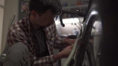 Genç adam stüdyo dairesine bisiklet aksesuarı takıyor. Adam evde bir bisiklet kuruyor. Erkek, ev çakıl bisikleti tamir ediyor. Bisikleti yeni sezon için tamir etme ve hazırlama kavramı