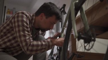 Genç adam stüdyo dairesine bisiklet aksesuarı takıyor. Adam evde bir bisiklet kuruyor. Erkek, ev çakıl bisikleti tamir ediyor. Bisikleti yeni sezon için tamir etme ve hazırlama kavramı