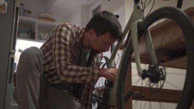 Genç adam stüdyo dairesine bisiklet aksesuarı takıyor. Adam evde bir bisiklet kuruyor. Erkek, ev çakıl bisikleti tamir ediyor. Bisikleti yeni sezon için tamir etme ve hazırlama kavramı