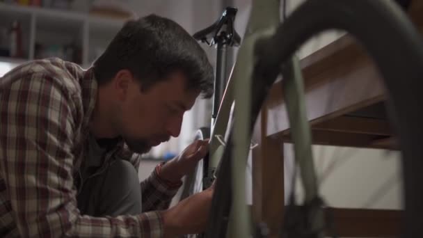 男人在家里修理自行车 男人在家里修理自行车 盖伊正在他们家调整他的周期 在一个小公寓里装自行车 在一间小工作室里为一个循环设定 — 图库视频影像