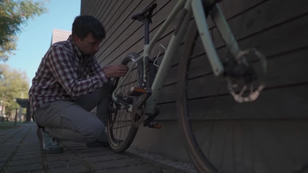 男は自転車の車輪を路上に小さなハンドポンプで汲み上げます 男は屋外で自転車のタイヤをポンプアップします 男はドイツの自転車駐車場でタイヤを膨らませている — ストック動画