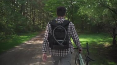 Bisiklet kilidi asılı sırt çantalı bir banliyö yolcusu kırık bir bisikleti onun yanına itiyor. Sırt çantası ve bisiklet kilidi olan genç bir adamın Almanya 'da bisiklet sürüşü.. 