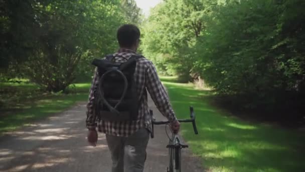 男人走在自行车旁边 背包上挂着自行车锁 后视镜年轻男子与背包和自行车锁在它推着自行车 一个提着背包的男人骑着自行车走在外面 — 图库视频影像