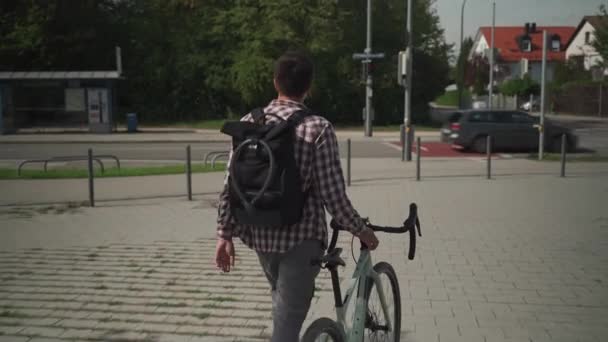 男人走在自行车旁边 背包上挂着自行车锁 后视镜年轻男子与背包和自行车锁在它推着自行车 一个提着背包的男人骑着自行车走在外面 — 图库视频影像