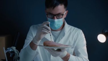Laboratuvar çalışanı et örneğine ilaç enjekte ediyor. Genetik olarak değiştirilmiş et. Yapay et ürünü, geleceğin gıda teknolojisi. GDO gıda konsepti. Erkek beslenme uzmanı gıda ürünlerini laboratuarda test ediyor.