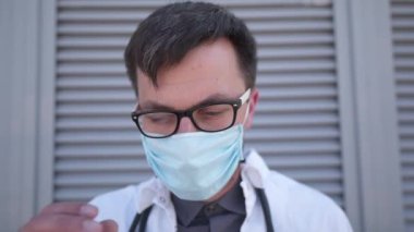 Gündüz vardiyasından sonra yorgun düşen doktor gergin bir gülümsemeyle maske ve gözlükleri çıkarır. Koronavirüsten ve pandemiden güvenli yaşam kavramı. Doktor maskesini düşürüyor ve hastanenin dışında gözlüklerini çıkarıyor.. 