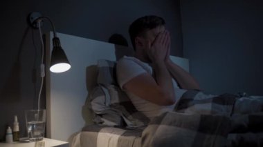 Tema uykusuzluk. Yorgun adam kötü uykudan muzdarip. Gece yatakta bir erkek gözlerini ovuşturuyor ve esniyor ve uyuyamıyor. Uykusuzluk konsepti. Uyku sorunları, aşırı çalışma. Uyku bozukluğu. 