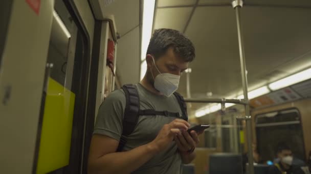 ドイツのミュンヘンの古い地下鉄で通勤中にマスクを身に着けている男性は携帯電話を使用します ミュンヘンのUバーン 地下鉄で通勤しながら 群集への社会的距離を保ちます コロナウイルスと公共交通機関 — ストック動画