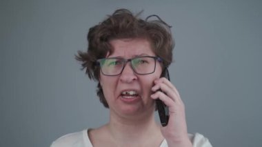 Diş yaralanması olan bir kadın, cep telefonuyla stüdyoda gri bir arkaplanı karşılaştırıyor. Dişinin korkunç bir diş ağrısı var ve doktoru arıyor. Sağlık sigortası. Diş hekimi kavramı. Diş hastalığı.. 