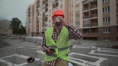 İnşaat sektörü çalışanı öğle arasında mesaj atıyor. Kask takan tamirci, şantiyede kahve molası sırasında akıllı telefon kullanıyor. Kasketli ve yelekli mimar inşaat alanında kahve içiyor.