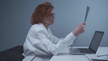 Kıdemli kadın doktor bir klinikte masada otururken hastaların MR 'larını muayene ediyor. Doktor, hastanedeki bilgisayarlı bilgisayarın arkasındaki tomografiyi inceliyor. Tıp, sağlık ve sinir cerrahisi teknolojisi kavramı. 
