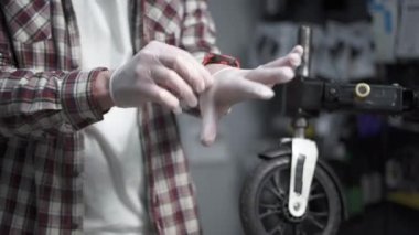 Bisiklet dükkanındaki tamirci bisiklet ve scooterları tamir etmeden önce elleri korumak için beyaz lateks koruyucu eldivenler giyer. Tamirci iş için eldiven takıyor. Erkek tamirci lateks iş eldivenleri giyer.