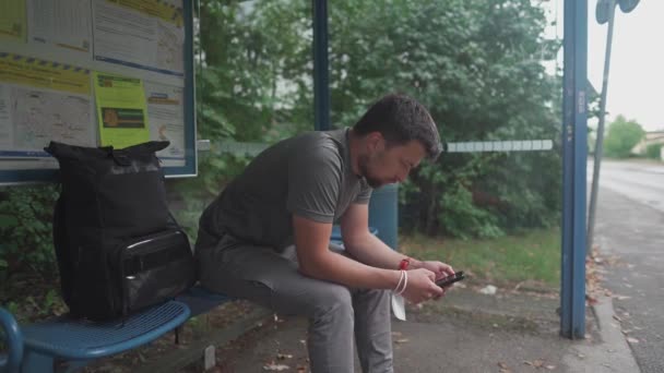 Hombre Sienta Parada Autobús Esperando Transporte Navegar Por Internet Teléfono — Vídeo de stock