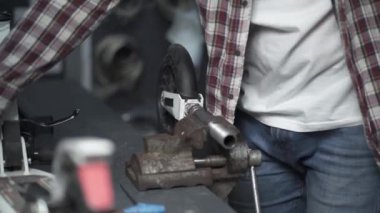 Profesyonel tamirci garajda çalışıyor. Yedek parçayı scooter 'dan kıskaçlamak ve onarmak için yedek mengene kullanıyor. Tamirci, scooter 'ın tekerleğini tamir ediyor. Beşikte sıkışmış ve atölyedeki İngiliz anahtarıyla kıvrılıyor.. 