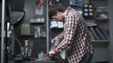 Profesyonel tamirci garajda çalışıyor. Yedek parçayı scooter 'dan kıskaçlamak ve onarmak için yedek mengene kullanıyor. Tamirci, scooter 'ın tekerleğini tamir ediyor. Beşikte sıkışmış ve atölyedeki İngiliz anahtarıyla kıvrılıyor.. 