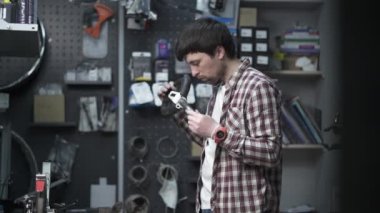 Erkek bir tamirci tamirhanede mobiletini tamir etmek için metal mengene kullanır. Atölyedeki motorun bir parçasını vises kullanarak kıskaçlayan bir tamirci. Bisiklet ve scooter tamir servisi. 