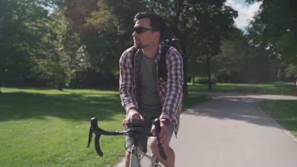 男はドイツの公園に乗っている間 自転車に乗って携帯電話上のGpsアプリケーションでコースをナビゲートします 自転車をバックパックでサイクリングし ハンドルバーにスマートフォンを使用してルートを作成します — ストック動画