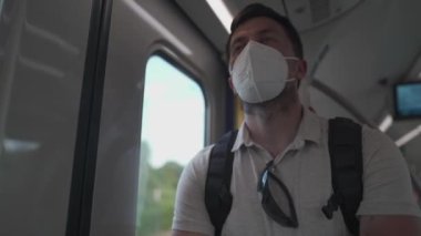 Almanya 'da pencerenin önünde duran banliyö trenindeki maskeli, üzgün, yorgun erkek yolcu. Yolcu taşımacılığı Münih 'te. Koronavirüs salgını sırasında seyahat etmek. Almanya 'da 9 avroluk kalabalık tren bileti. 