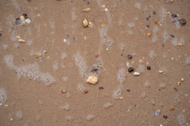 Sahilde dalgalı köpüklü sayısız çakıl taşı. Seçici odak noktaları