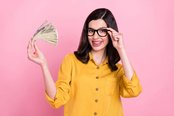 Φωτογραφία από αστεία μελαχρινή hairdo χιλιετή κυρία δείχνουν χρήματα φορούν κίτρινο πουκάμισο γυαλιά που απομονώνονται σε ροζ φόντο χρώμα — Φωτογραφία Αρχείου