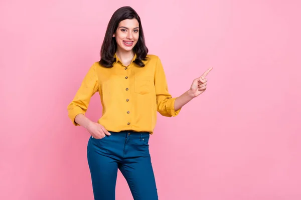 Foto av optimistisk brunett frisyr ung dam punkt tomt utrymme bära gul skjorta isolerad på rosa färg bakgrund — Stockfoto