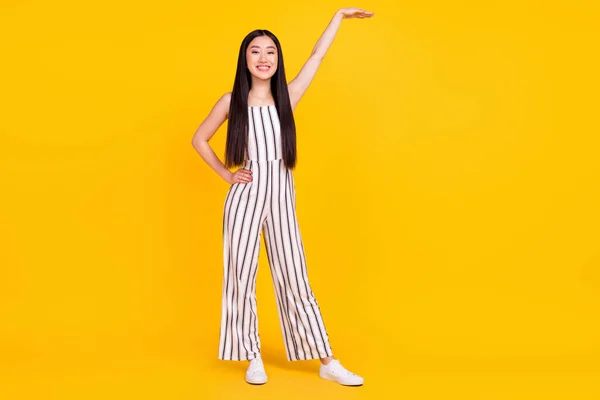 Tamanho total do corpo foto menina sorrindo em listrado geral mostrando altura com mão isolado vibrante cor amarela fundo — Fotografia de Stock