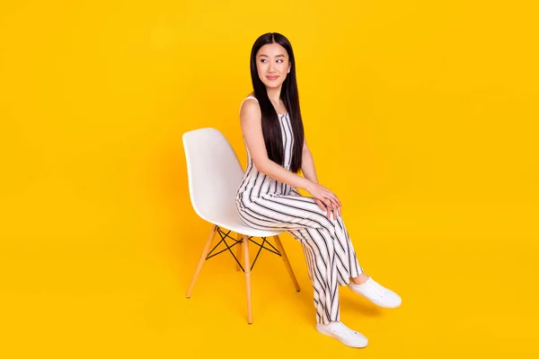 Volledige lengte body size foto jong meisje zitten op stoel dragen casual algehele op zoek copyspace glimlachen geïsoleerde levendige gele kleur achtergrond — Stockfoto
