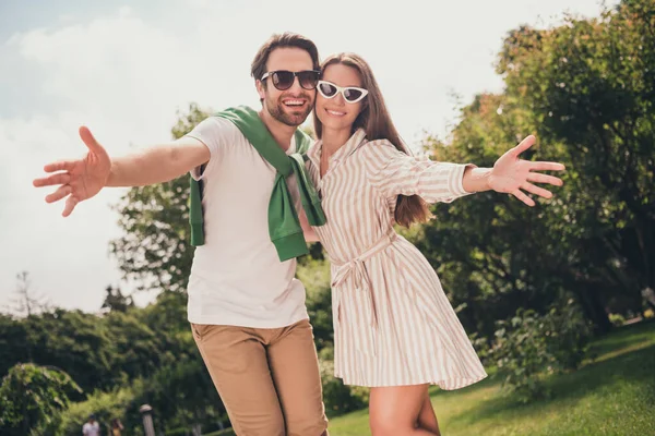 Portret fotograficzny młoda para uśmiechnięta z otwartymi rękami na spotkanie z przyjaciółmi noszącymi okulary przeciwsłoneczne — Zdjęcie stockowe