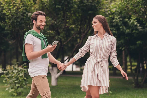 Foto portriat jovem casal sorrindo andando no parque verde de mãos dadas cara usando smartphone olhando no mapa — Fotografia de Stock