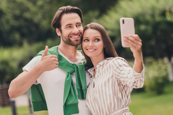 Photo de jeune couple joyeux heureux sourire positif tirer selfie smartphone gars montrer pouce vers le haut comme fin en plein air — Photo