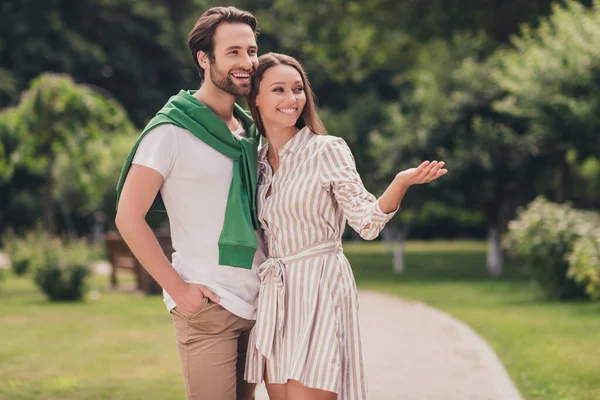Foto de jovem casal atraente feliz sorriso positivo data sentimentos menina demonstrar mão espaço vazio andar ao ar livre — Fotografia de Stock