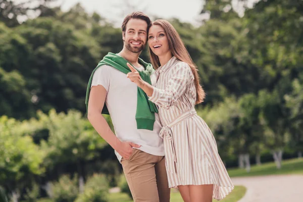 Foto de joven alegre pareja feliz sonrisa positiva chica punto indican dedo curioso interesado abrazo caminar al aire libre —  Fotos de Stock